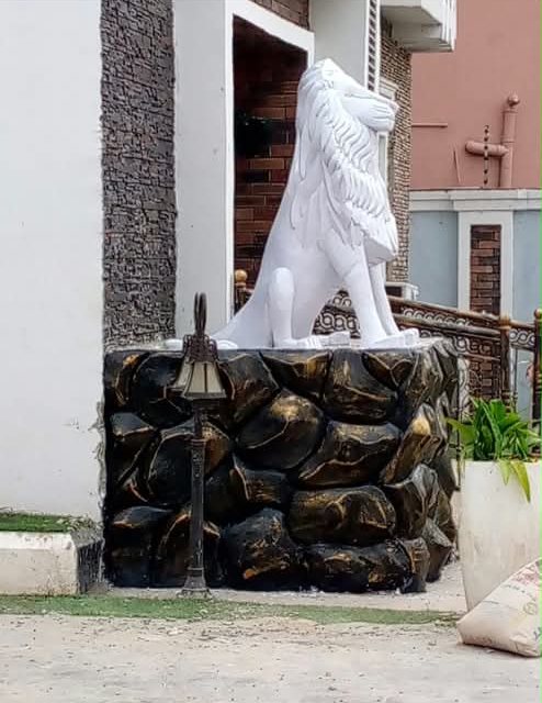 White lion statue on a black-and-gold rock-textured pedestal at a house entrance
